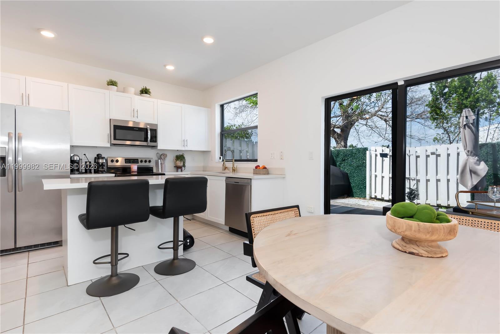 A modern kitchen features white cabinetry, stainless steel appliances, a breakfast bar, and sliding doors — 9949 SW 228th Ter, Miami FL 33190, MIAMI, FL