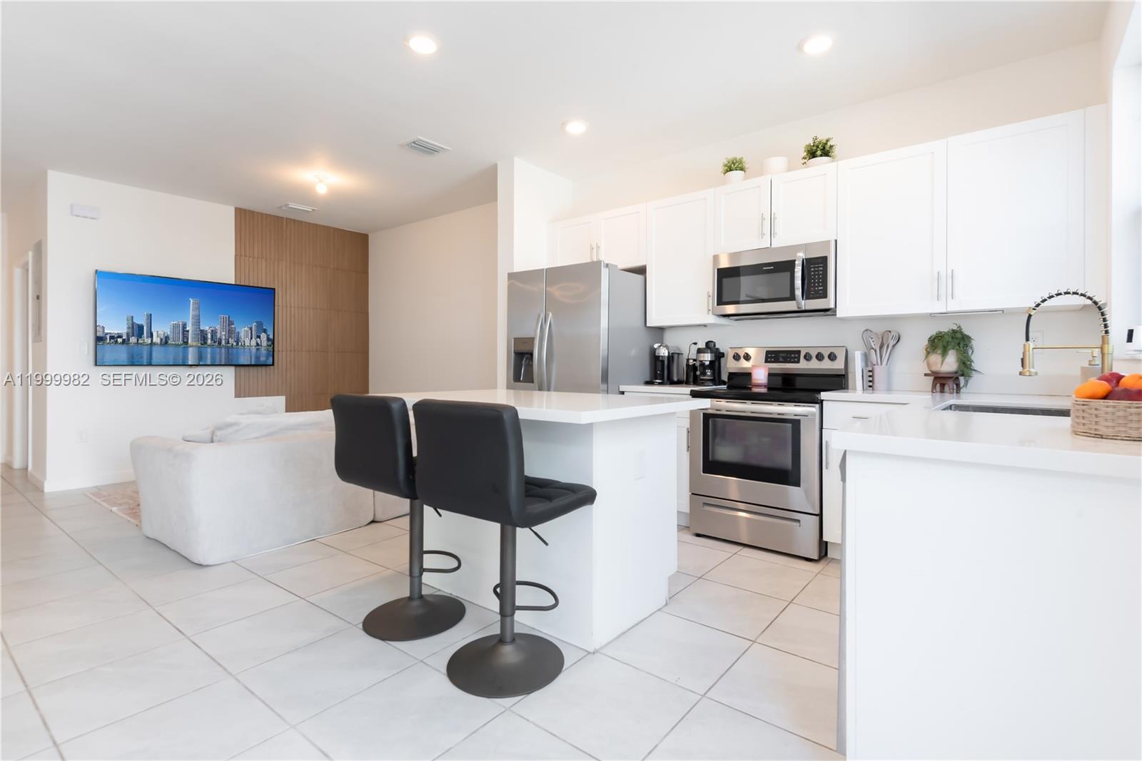 A modern kitchen with white cabinets and stainless steel appliances opens into a living area — 9949 SW 228th Ter, Miami FL 33190, MIAMI, FL