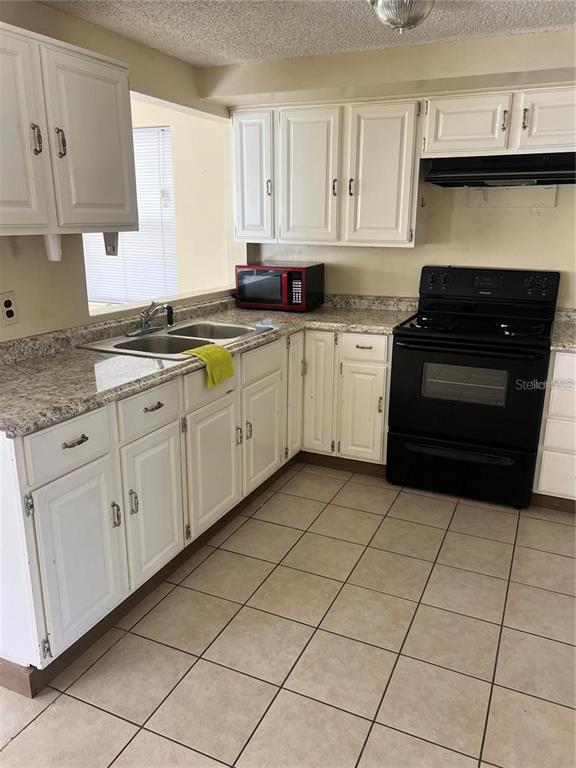 A kitchen features white cabinets, granite-look countertops, a black stove, and light-colored floor tiles — 7438 COVENTRY DRIVE, PORT RICHEY, FL