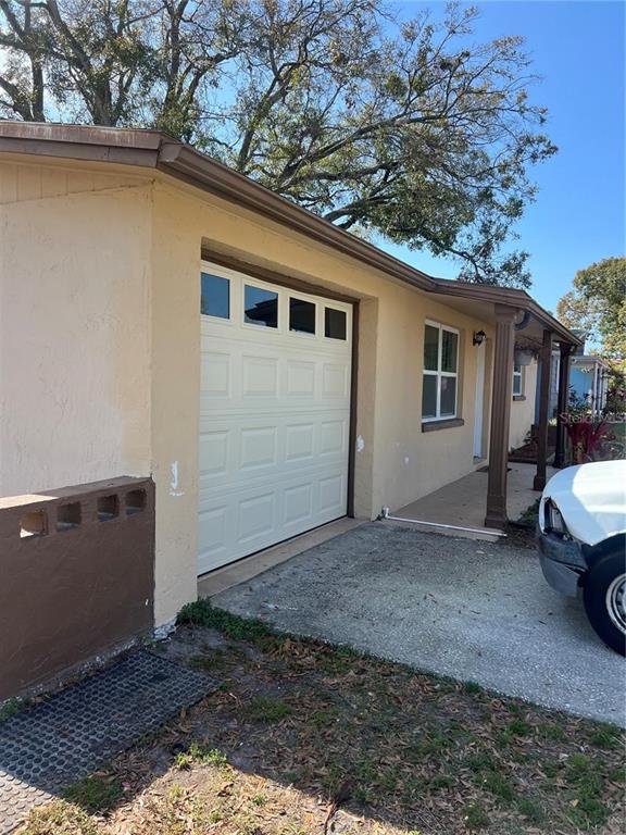 A beige house exterior features a white garage door, a covered porch, and a driveway — 7438 COVENTRY DRIVE, PORT RICHEY, FL
