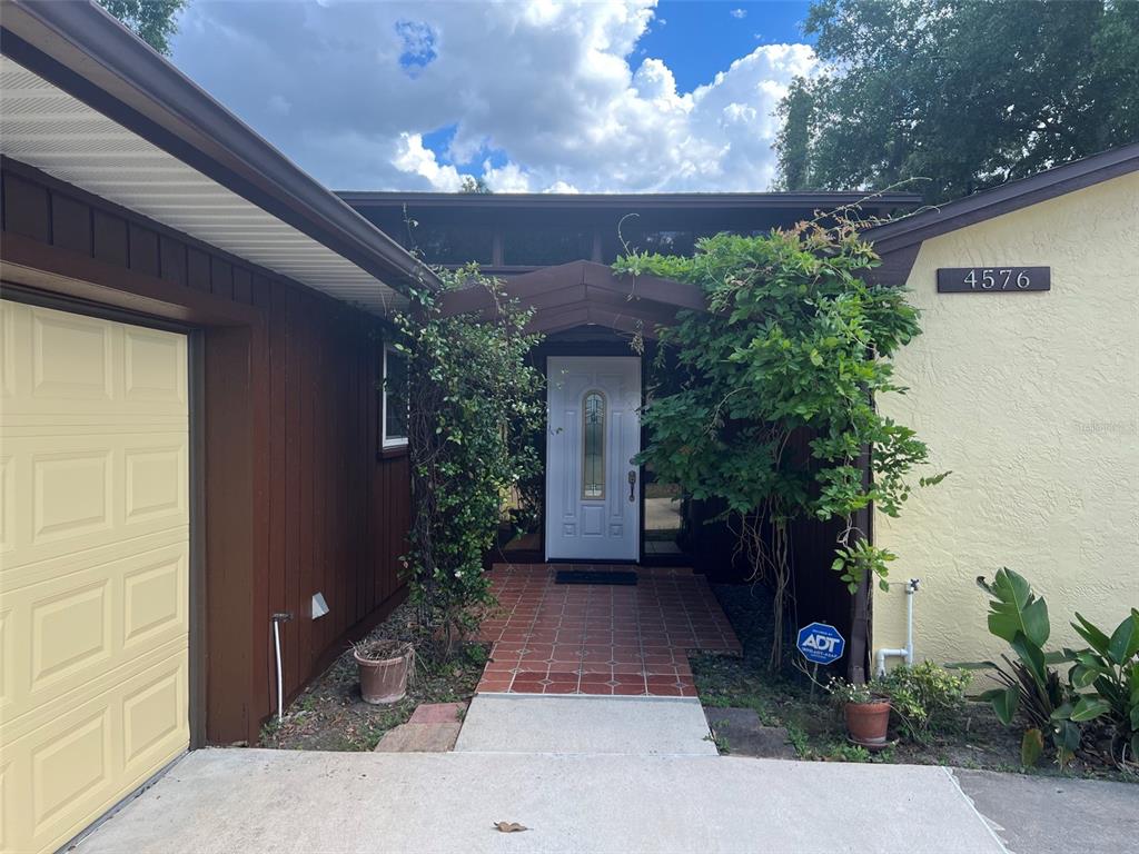 A front entrance features a white door, a tiled walkway, and overgrown vines on both sides — 4576 NORTH LANE, ORLANDO, FL