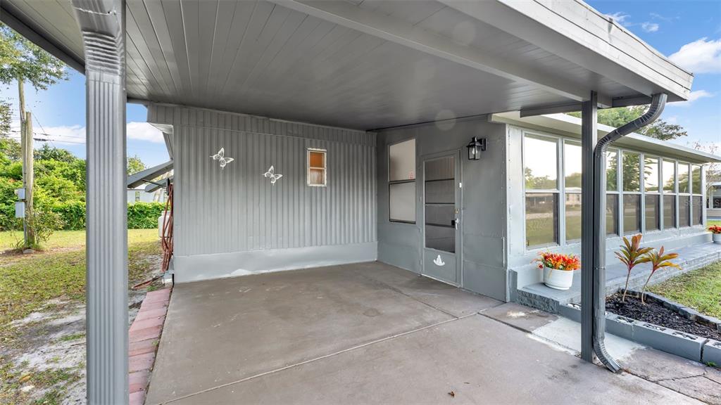 A gray covered carport features a concrete floor, a side door, and exterior wall decorations — 203 JANET LANE, LAKELAND, FL