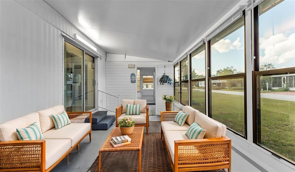 A sunroom features two wicker sofas, a coffee table, and large windows overlooking a yard — 203 JANET LANE, LAKELAND, FL