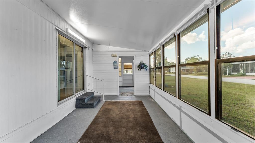 A sunroom features white walls, a brown rug, and large windows overlooking a grassy yard — 203 JANET LANE, LAKELAND, FL