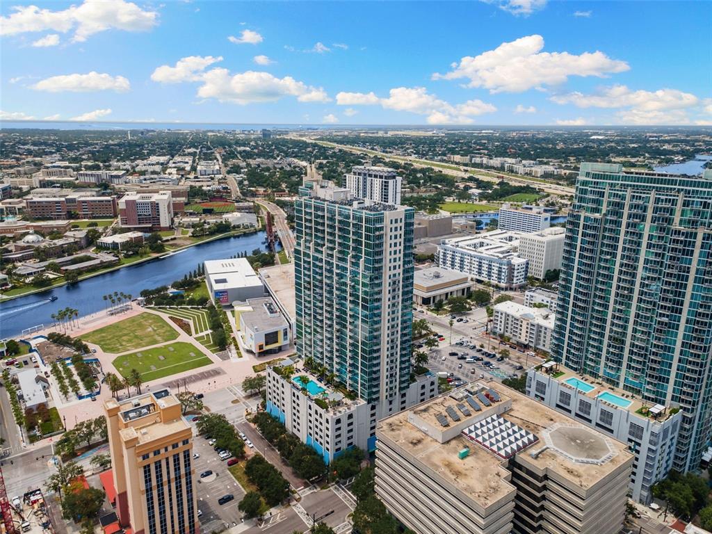 An aerial view shows a tall glass skyscraper surrounded by urban buildings and a river — 777 N ASHLEY DRIVE UNIT 2514, TAMPA, FL
