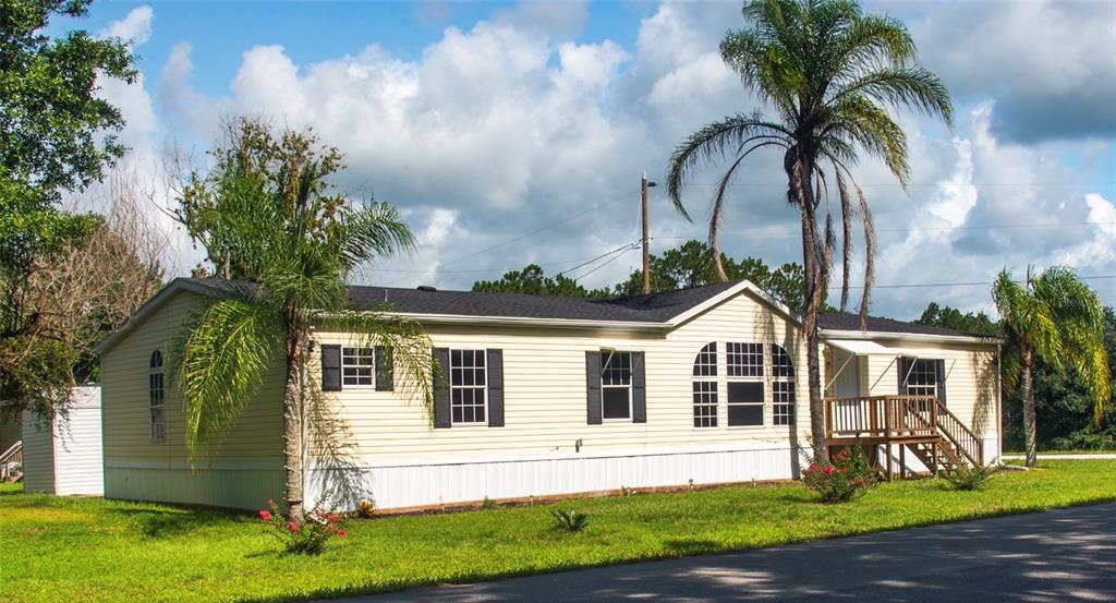 A single-story manufactured home with light siding, dark shutters, and palm trees in the yard — 219 BALLARD ROAD, AVON PARK, FL