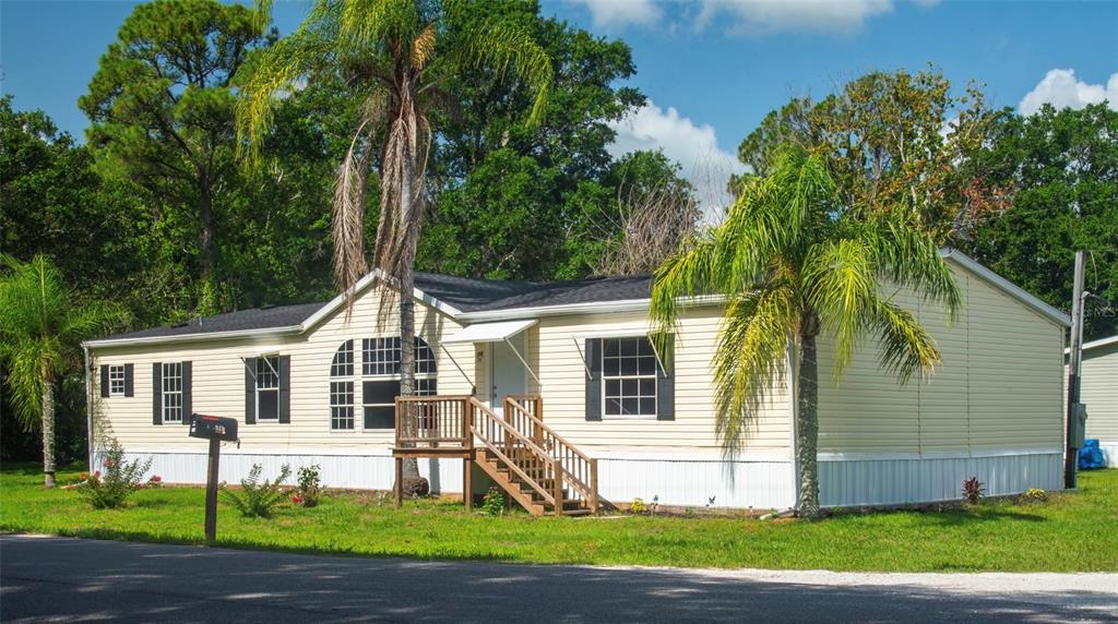 A single-story manufactured home with light yellow siding, a wooden front deck, and palm trees — 219 BALLARD ROAD, AVON PARK, FL