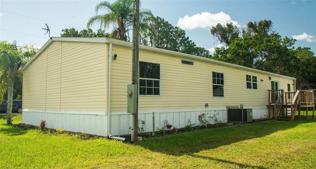 The exterior of a light yellow manufactured home features vinyl siding and a wooden deck — 219 BALLARD ROAD, AVON PARK, FL