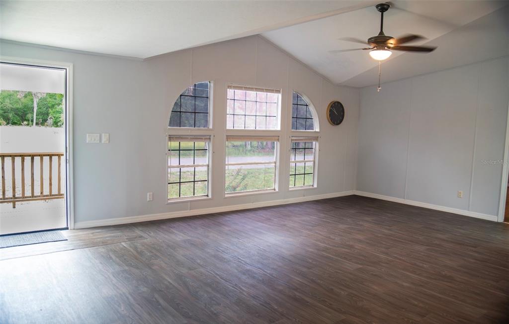 A living room with vaulted ceilings, dark wood-look flooring, and three arched windows — 219 BALLARD ROAD, AVON PARK, FL