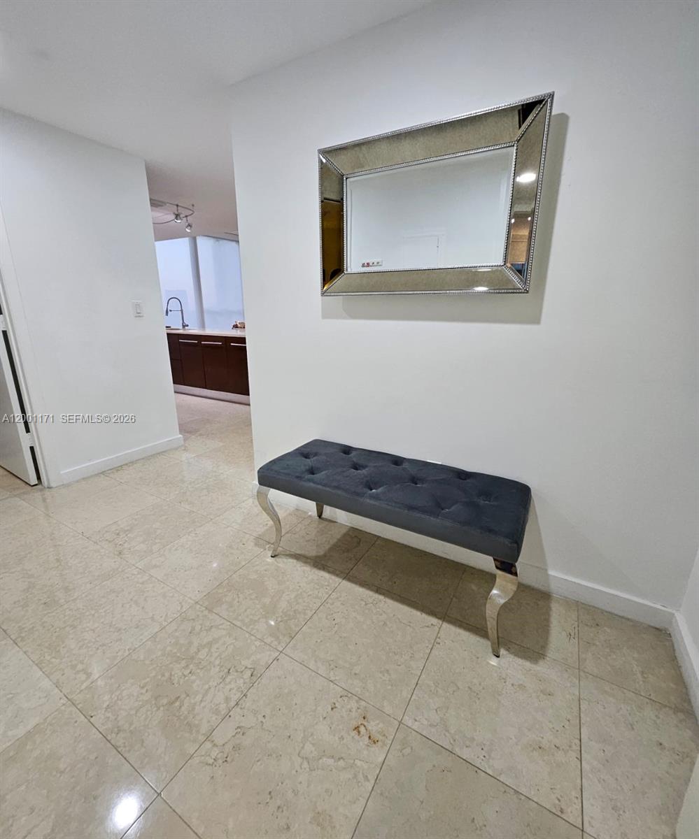 A hallway features a tufted grey bench beneath a rectangular mirror on a white wall — 475 Brickell Ave # 2115, Miami FL 33131, MIAMI, FL