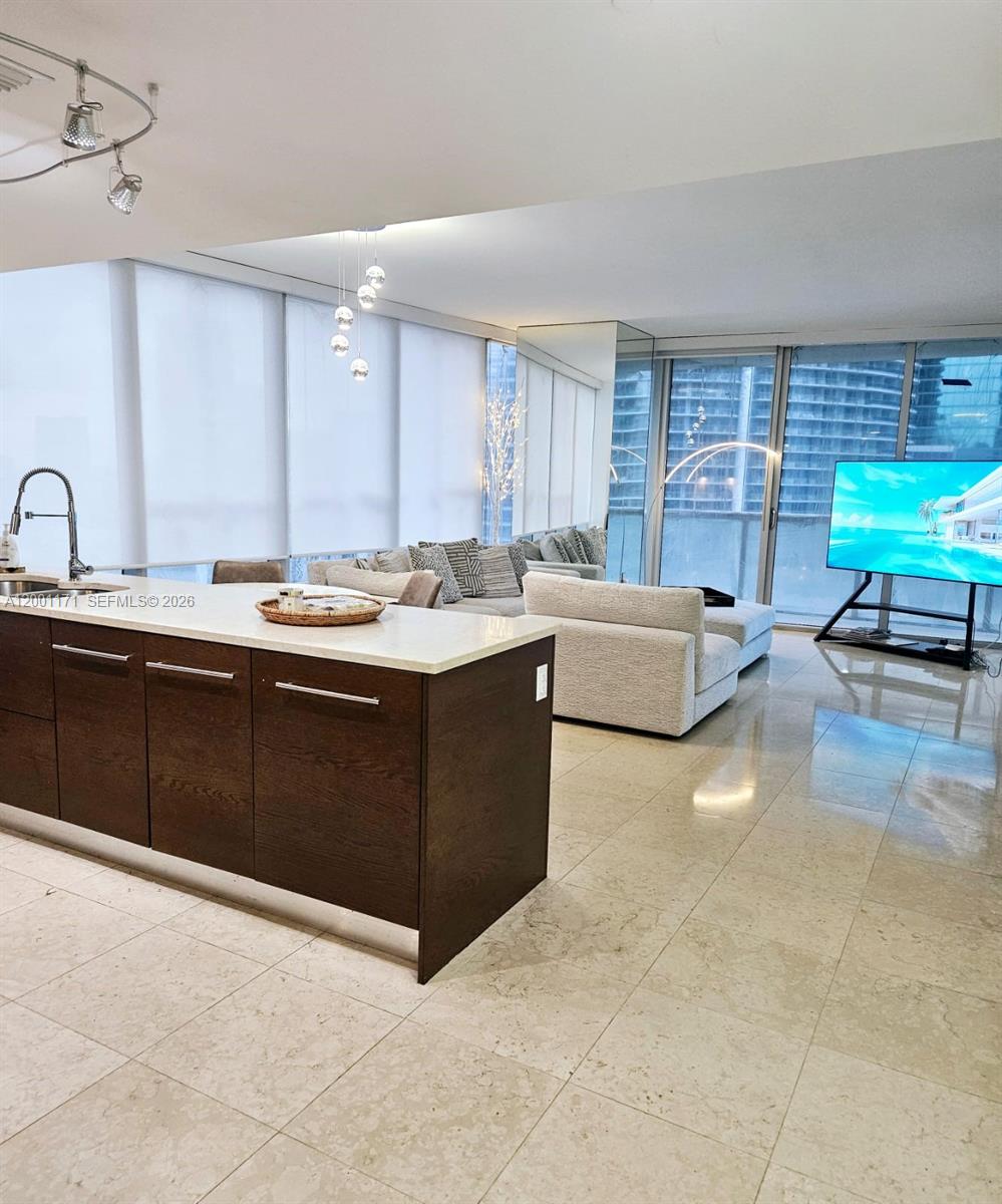 A modern kitchen island with dark wood cabinets sits before an open-concept living area — 475 Brickell Ave # 2115, Miami FL 33131, MIAMI, FL