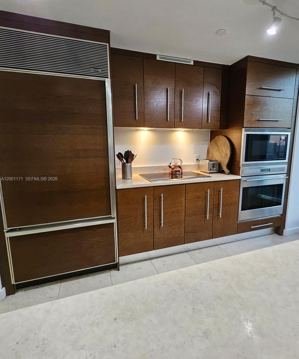 A kitchen features dark wood cabinetry, stainless steel appliances, and light-colored countertops — 475 Brickell Ave # 2115, Miami FL 33131, MIAMI, FL