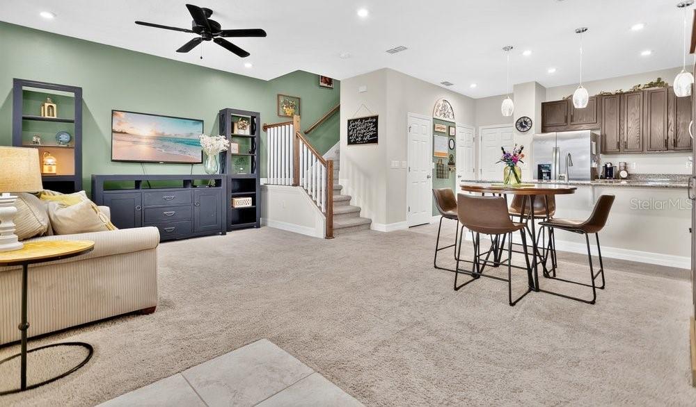 An open-concept living room and kitchen area with a staircase, carpeted floors, and green walls — 2145 VALENCIA BLOSSOM STREET, CLERMONT, FL