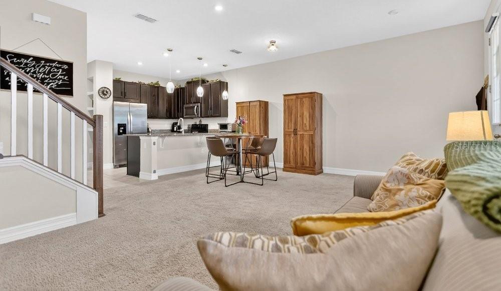 An open-concept living room and kitchen area with dark wood cabinets and carpeted flooring — 2145 VALENCIA BLOSSOM STREET, CLERMONT, FL