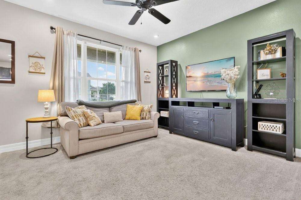 A living room features a beige sofa, a dark media console, and two tall bookshelves — 2145 VALENCIA BLOSSOM STREET, CLERMONT, FL