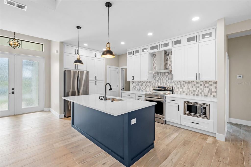 A kitchen features a dark blue island, white cabinetry, stainless steel appliances, and wood-look flooring — 2523 DIXON TERRACE, PORT CHARLOTTE, FL