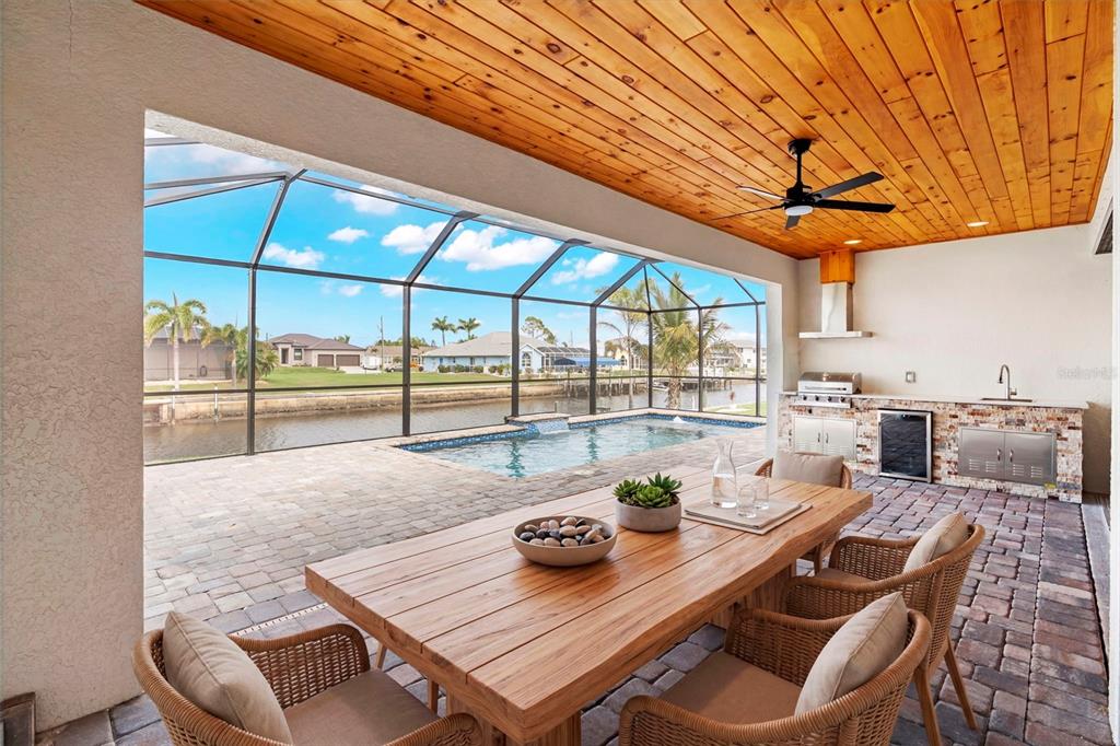 A covered patio features a wooden ceiling, outdoor kitchen, dining table, and a screened-in pool — 2523 DIXON TERRACE, PORT CHARLOTTE, FL