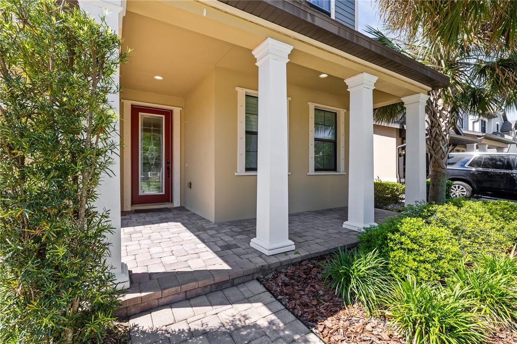 A covered front porch with white columns, a red door, and paver flooring — 12476 TIBBETTS STREET, ODESSA, FL