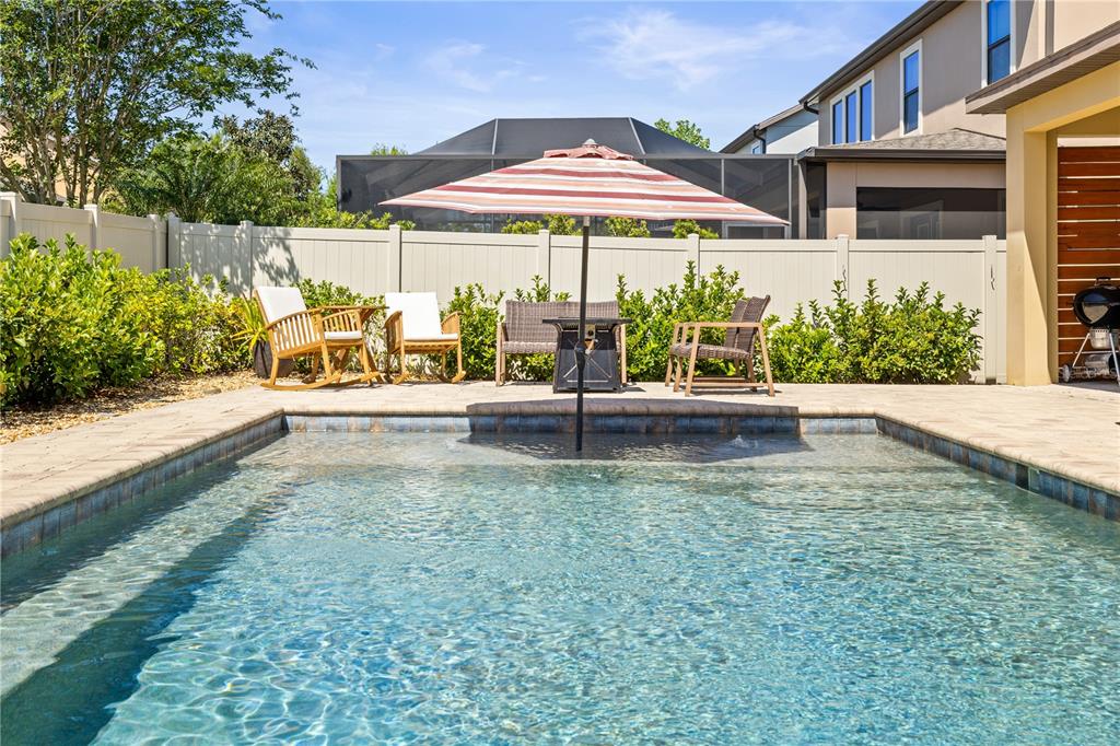 A swimming pool with a central umbrella and patio furniture sits in a fenced backyard — 12476 TIBBETTS STREET, ODESSA, FL