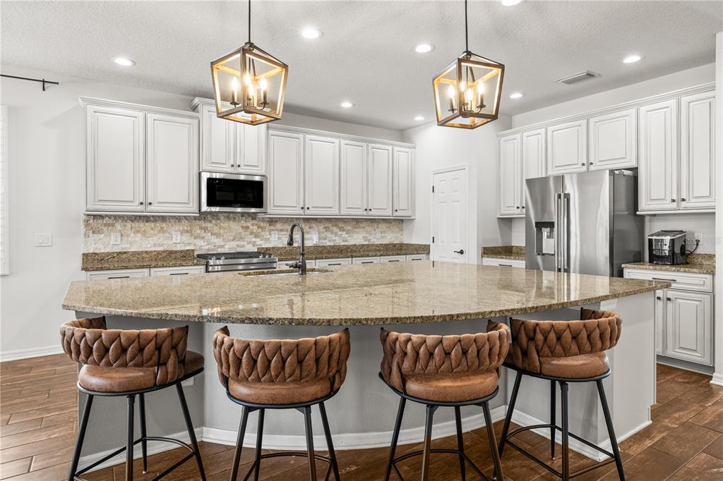 A kitchen features white cabinets, granite countertops, a large island, and four brown bar stools — 12476 TIBBETTS STREET, ODESSA, FL