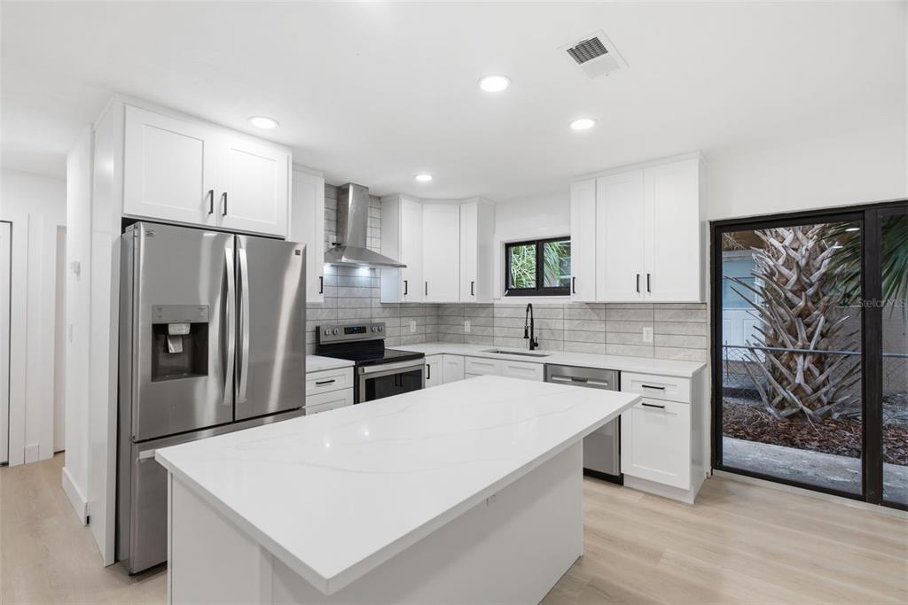 A modern kitchen features white cabinets, stainless steel appliances, a quartz island, and tile backsplash — 595 PINE STREET, SAFETY HARBOR, FL