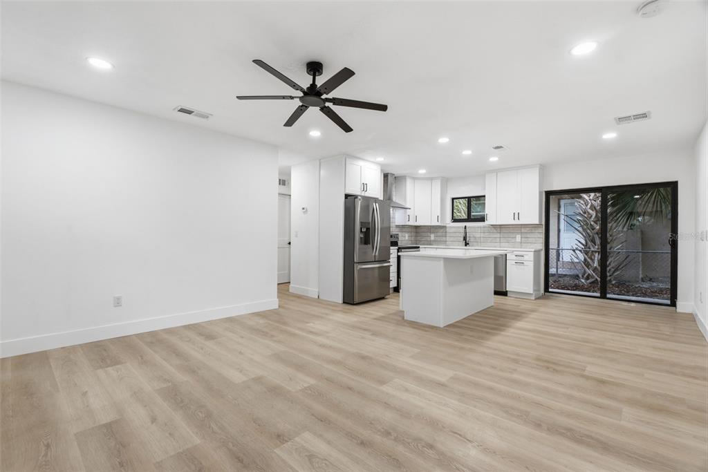 A bright, open-concept kitchen and living area with white cabinets, stainless appliances, and wood flooring — 595 PINE STREET, SAFETY HARBOR, FL