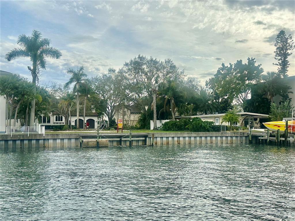 A waterfront view of a canal with a bulkhead, palm trees, and residential houses — 52 SANDPIPER ROAD, TAMPA, FL
