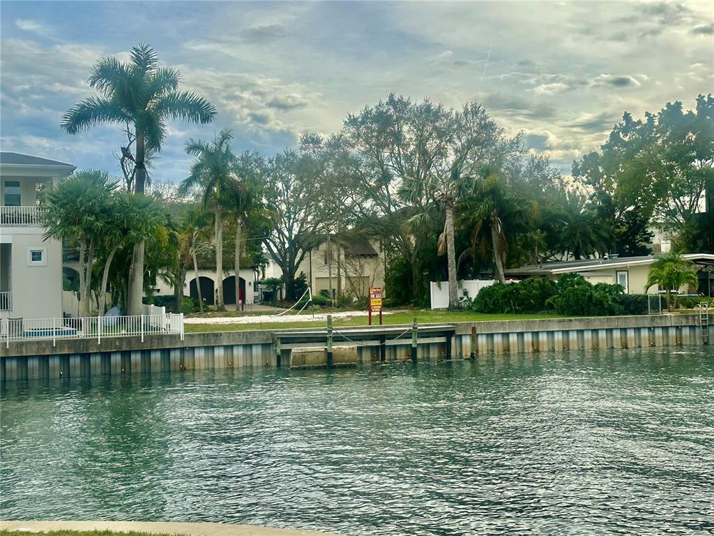 A vacant waterfront lot features a seawall, mature trees, and a for sale sign — 52 SANDPIPER ROAD, TAMPA, FL