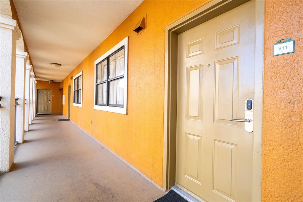 An outdoor apartment hallway with orange walls, tan doors, and a numbered unit sign — 12527 FLORIDAYS RESORT DRIVE UNIT 611-E, ORLANDO, FL