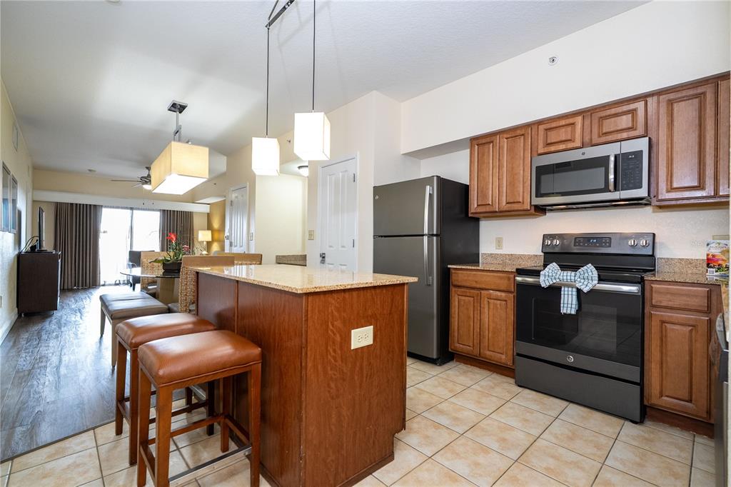 A kitchen with wood cabinets, stainless steel appliances, and a granite-topped island with two stools — 12527 FLORIDAYS RESORT DRIVE UNIT 611-E, ORLANDO, FL