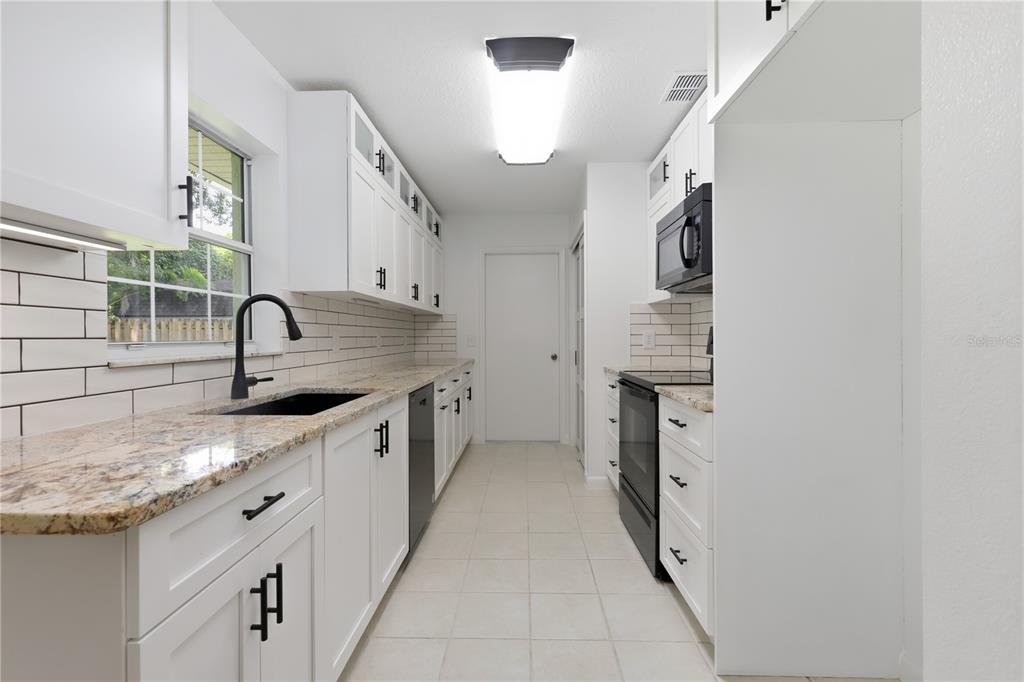 A galley kitchen features white cabinets, granite countertops, black appliances, and a subway tile backsplash — 2020 LEMON STREET, DELAND, FL