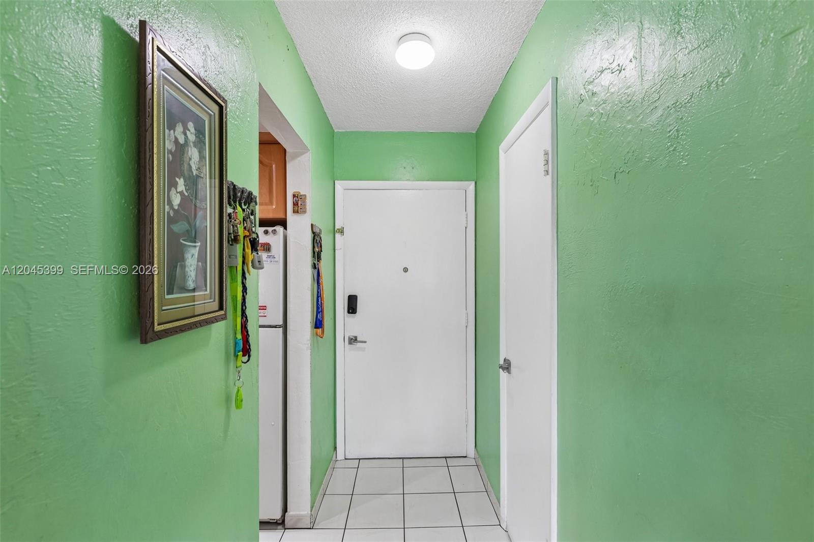 A hallway with bright green walls, white tile flooring, and a white entry door — 1300 W 53rd St # 25, Hialeah FL 33012, HIALEAH, FL