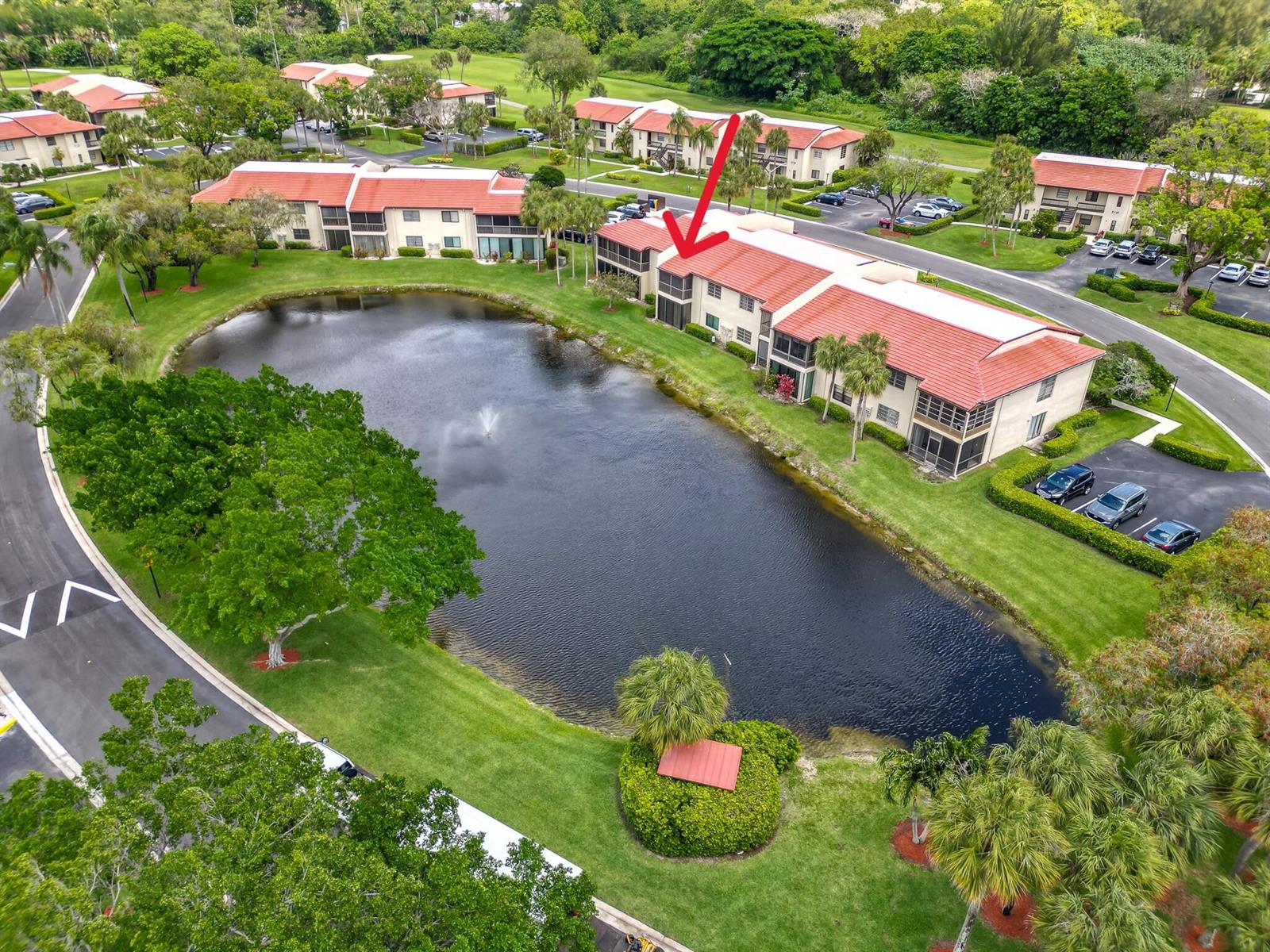 An aerial view shows a multi-story apartment building with a red roof beside a pond — 21218 Lago Circle # H, Boca Raton FL 33433, BOCA RATON, FL