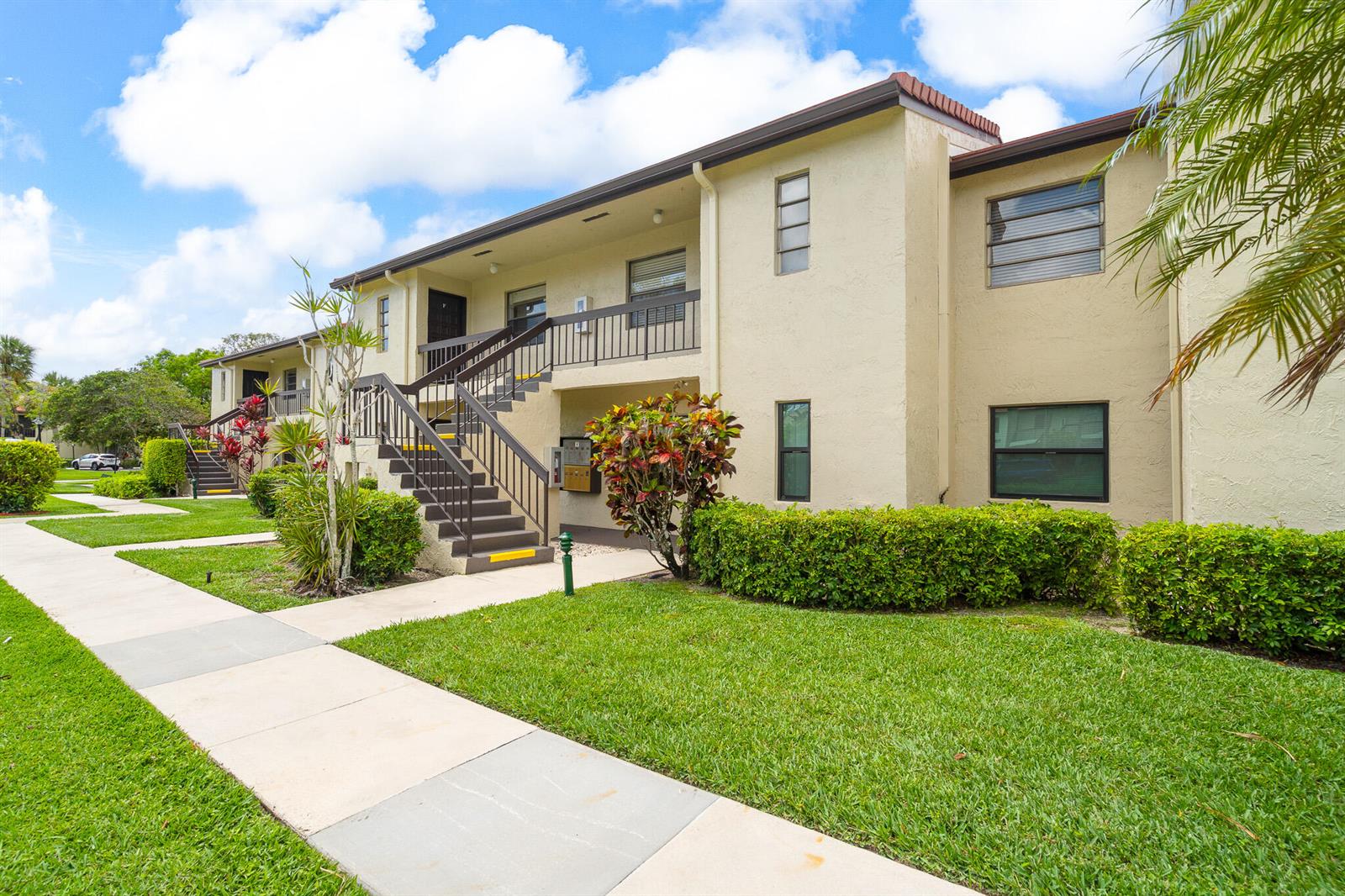 A two-story apartment building with beige stucco walls, brown railings, and a landscaped front lawn — 21218 Lago Circle # H, Boca Raton FL 33433, BOCA RATON, FL