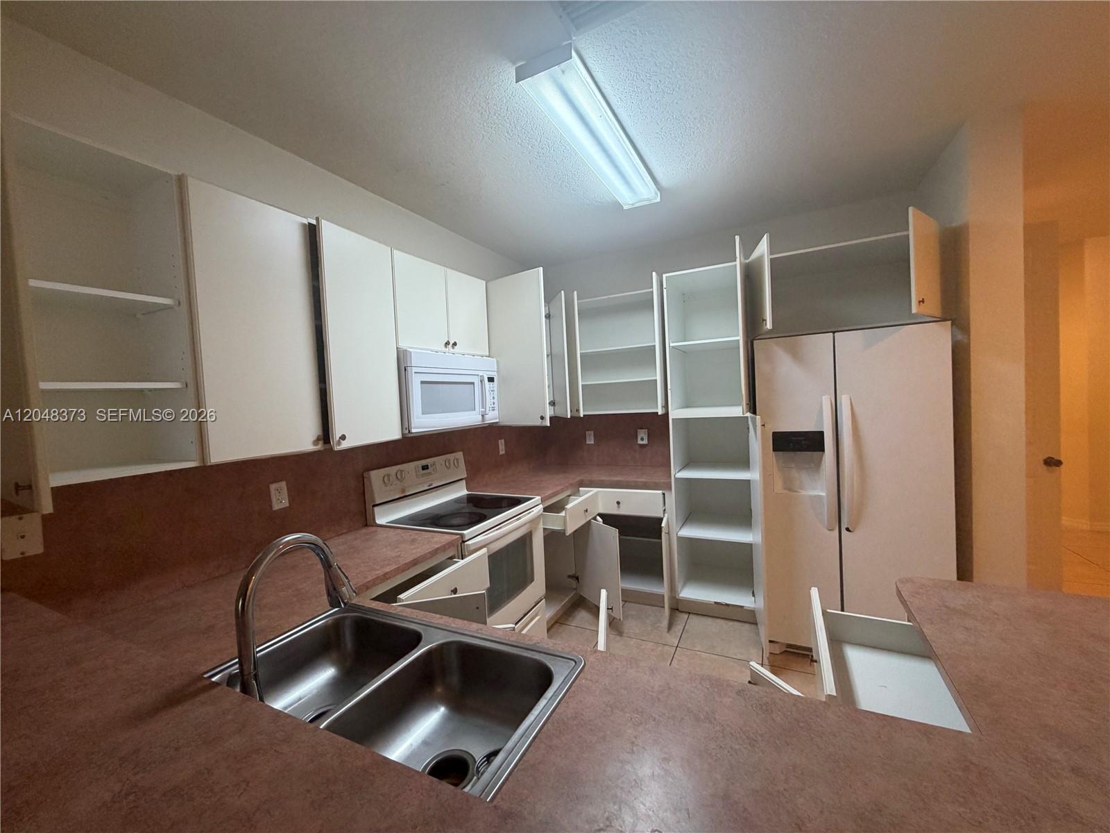 A kitchen features white cabinets, a stainless steel sink, and pink laminate countertops — 666 NE 35th Ave, Homestead FL 33033, HOMESTEAD, FL