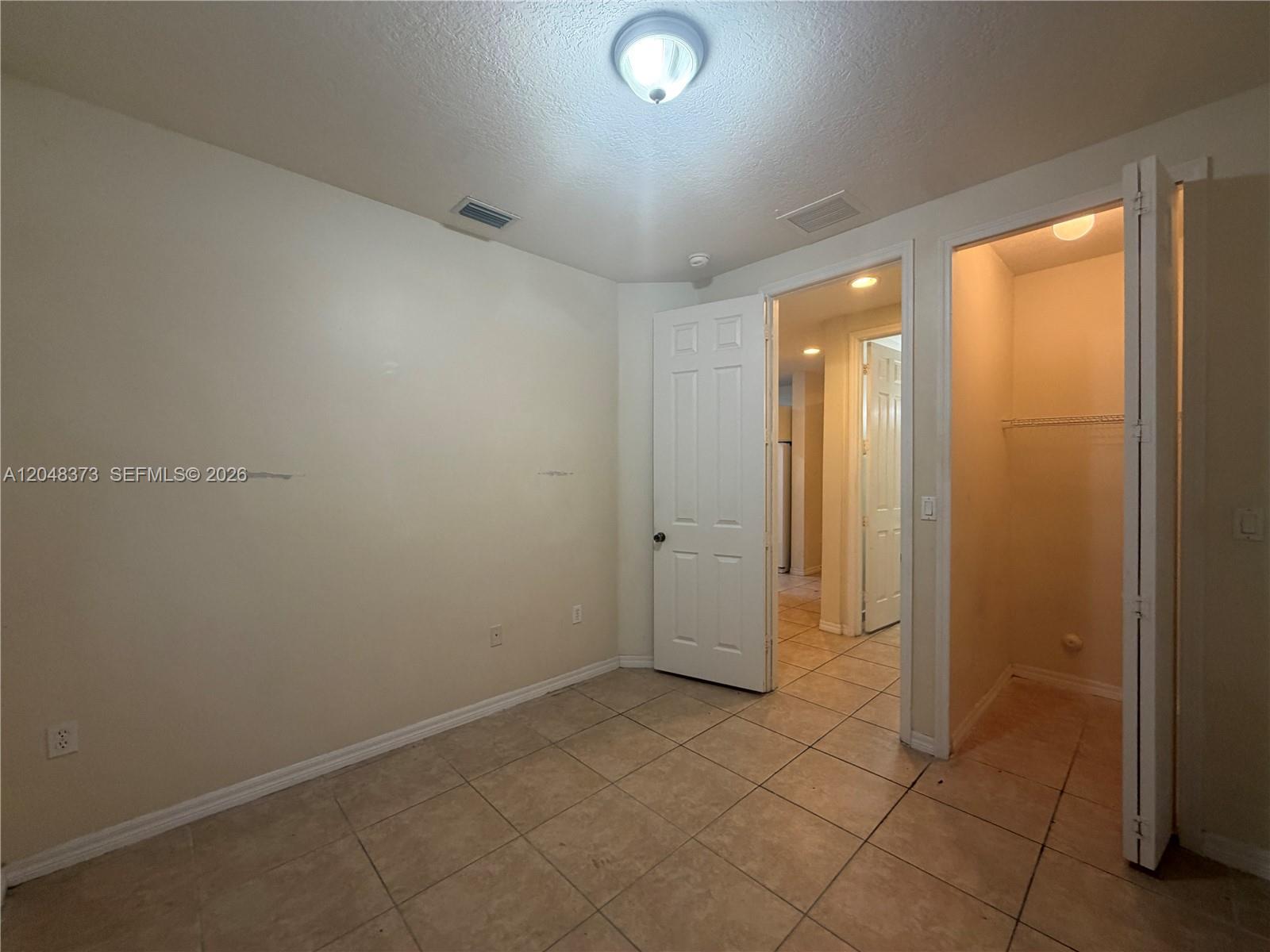 An empty room features beige tile flooring, a white door, and an open closet — 666 NE 35th Ave, Homestead FL 33033, HOMESTEAD, FL