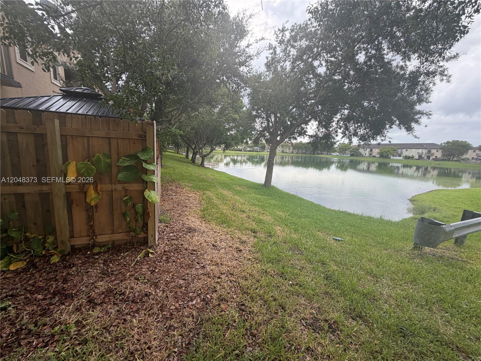 A wooden fence stands beside a grassy lawn overlooking a lake with trees — 666 NE 35th Ave, Homestead FL 33033, HOMESTEAD, FL