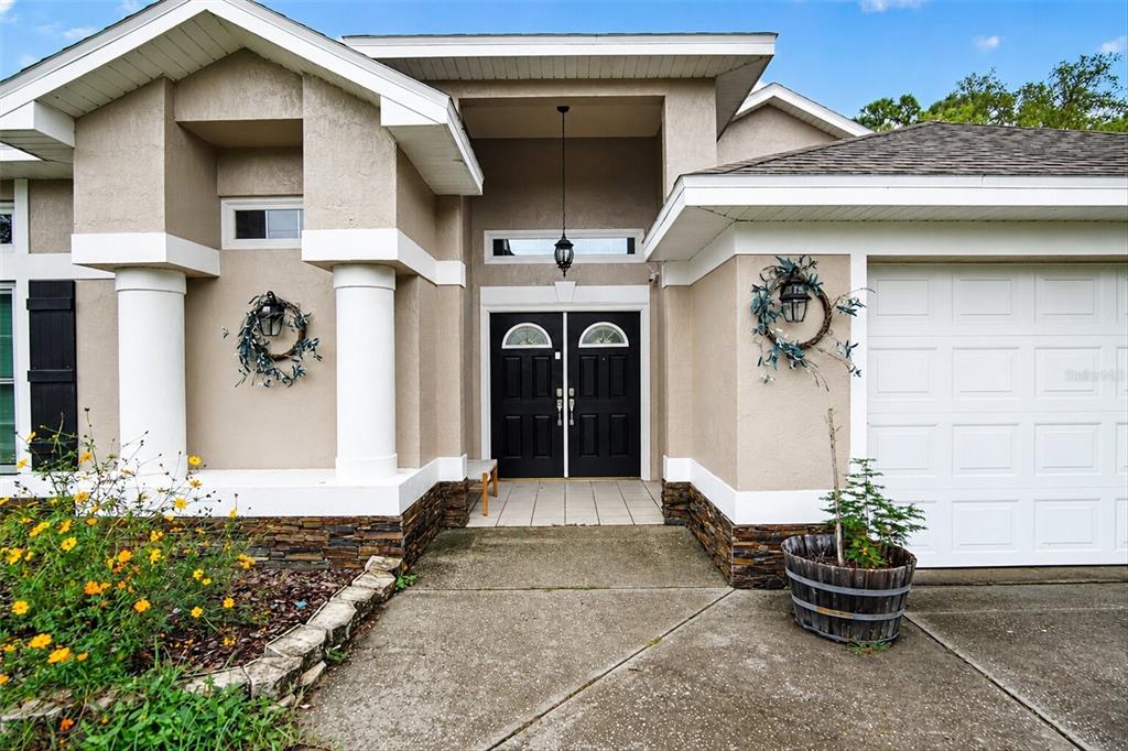 The exterior of a tan house features a double front door, white columns, and stone accents — 9123 MAVIS ROAD, WEEKI WACHEE, FL