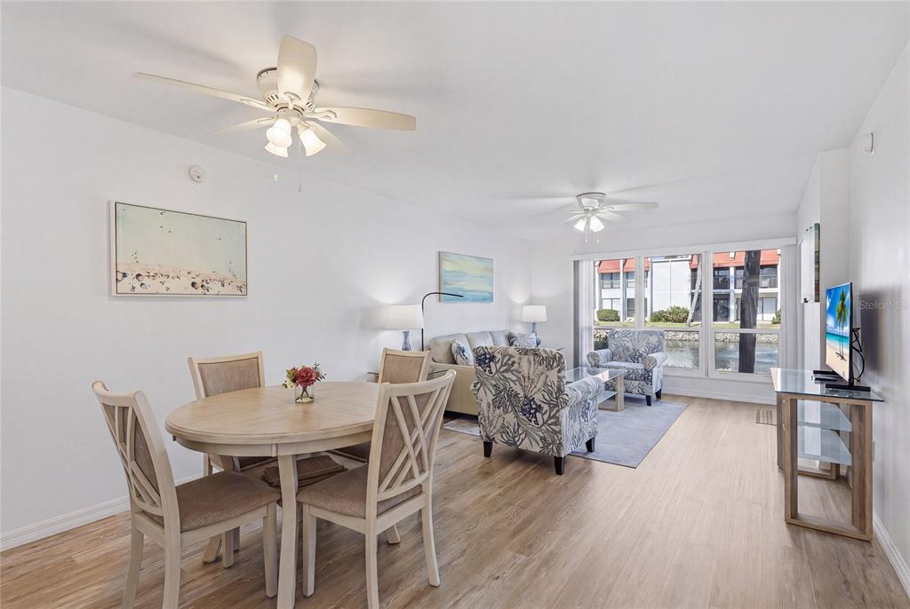 A bright living and dining area features light wood flooring, ceiling fans, and water views — 1801 GULF DRIVE N UNIT 183, BRADENTON BEACH, FL