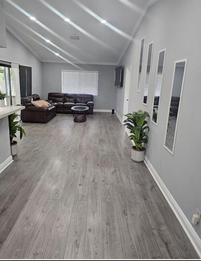A living room features gray wood-look flooring, gray walls, a brown sectional, and wall-mounted mirrors — 750 SW 55th Avenue, Margate FL 33068, MARGATE, FL