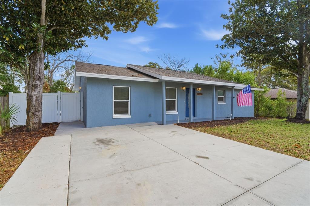 A single-story blue house with a concrete driveway, covered porch, and an American flag — 32730 BLOSSOM LANE, LEESBURG, FL