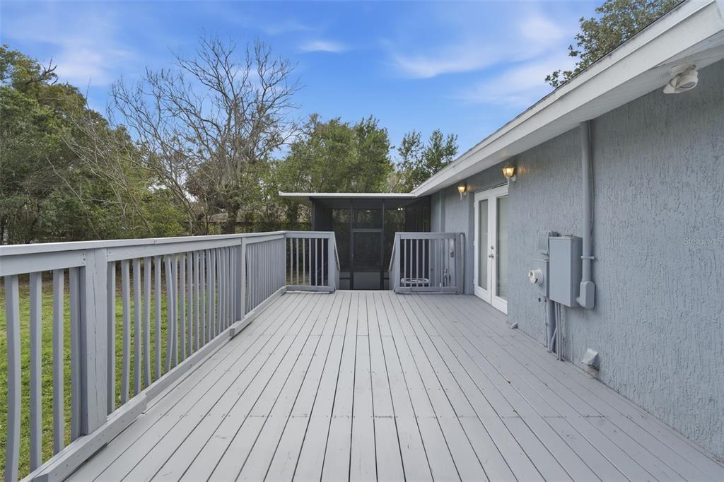 A gray wooden deck with railings leads to a screened-in porch and a house exterior — 32730 BLOSSOM LANE, LEESBURG, FL