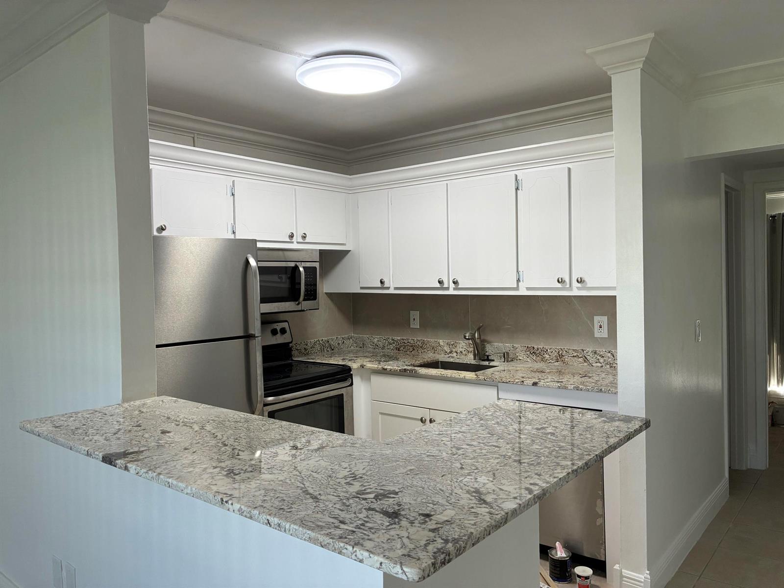 A kitchen features white cabinets, granite countertops, stainless steel appliances, and a breakfast bar — 650 Horizons Avenue E # 107, Boynton Beach FL 33435, BOYNTON BEACH, FL