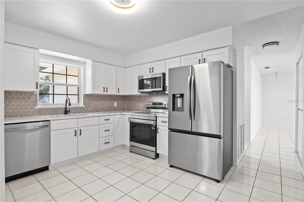 A kitchen features white cabinets, stainless steel appliances, a tiled backsplash, and white floor tiles — 776 MOCKINGBIRD LANE, DELAND, FL