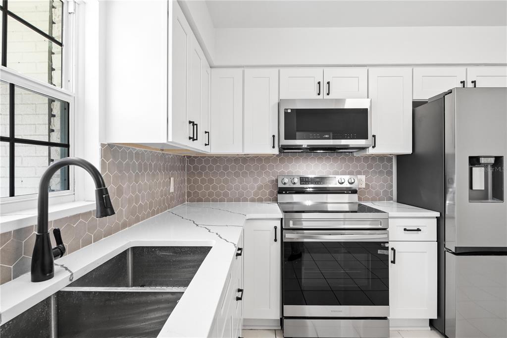 A kitchen features white cabinets, quartz countertops, a stainless steel stove, and a hexagonal backsplash — 776 MOCKINGBIRD LANE, DELAND, FL