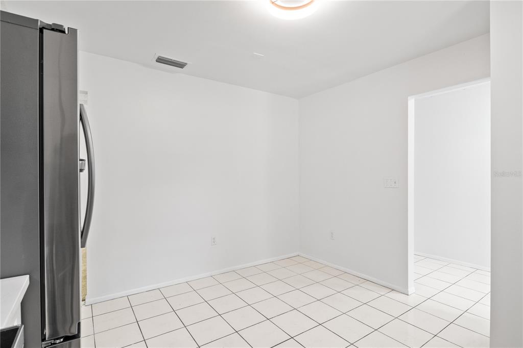 A bright, empty kitchen dining area features white walls, white tile flooring, and a refrigerator — 776 MOCKINGBIRD LANE, DELAND, FL
