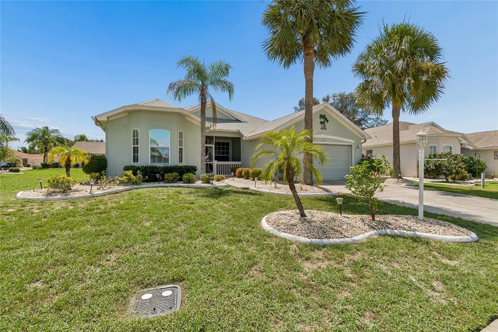 A single-story house with a light green exterior, a two-car garage, and several palm trees — 1119 VILLEROY DRIVE, SUN CITY CENTER, FL
