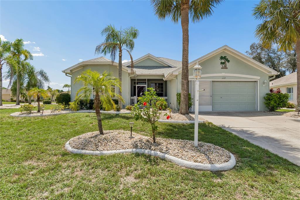 A light green single-story house with a garage, palm trees, and a landscaped front yard — 1119 VILLEROY DRIVE, SUN CITY CENTER, FL