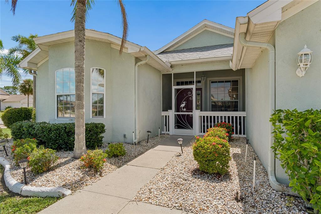 The exterior of a light green house features a concrete walkway leading to a screened entryway — 1119 VILLEROY DRIVE, SUN CITY CENTER, FL