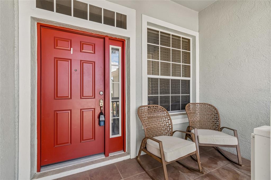 A red front door with a side window and two wicker chairs on a porch — 1119 VILLEROY DRIVE, SUN CITY CENTER, FL